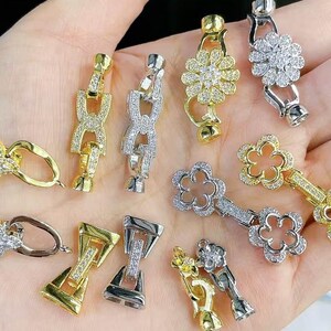 Puede incluir: Surtido de cierres de metal en tono plateado y dorado con detalles de strass transparentes. Los cierres son de varias formas, incluyendo flores, círculos y cuadrados.