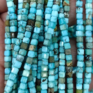 Può includere: Una collana di perle di turchese, ogni perla è di forma quadrata con una finitura sfaccettata. Le perle sono di colore blu chiaro con inclusiones marroni e verdi.