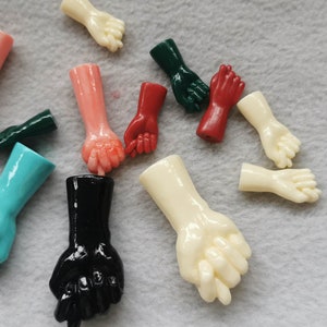 Könnte beinhalten: Sortiment kleiner Plastikhände in verschiedenen Farben, darunter Rot, Grün, Blau, Schwarz und Weiß. Die Hände sind in verschiedenen Posen, darunter Fäuste, offene Handflächen und Zeigefinger.