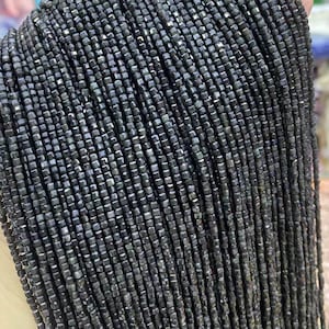 May include: A strand of dark gray square beads with a metallic sheen. The beads are small and uniform in size.