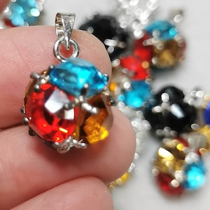 May include: A silver pendant with a round, faceted gemstone. The gemstone is made up of three smaller gemstones, one red, one orange, and one blue.