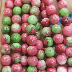 May include: A strand of round, green and pink beads with white marbling. The beads are smooth and glossy.