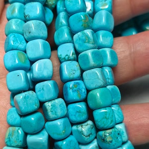 Può includere: Una collana di perle di turchese, ogni perla ha una forma quadrata con bordi arrotondati. Le perle sono di un colore blu-verde vibrante con variazioni naturali nella pietra.