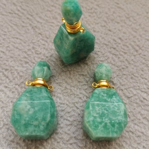 Könnte beinhalten: Drei grüne Aventurin-Edelsteinflaschen mit goldenen Kappen und Schlaufen. Die Flaschen sind facettiert und haben ein natürliches, erdiges Aussehen.