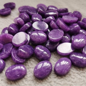 May include: A pile of purple oval-shaped gemstones. The stones are smooth and have a slight shimmer to them.