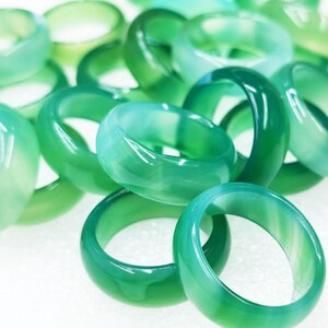 Op de afbeelding: Een verzameling doorschijnende groene ringen. De ringen variëren in groentinten, van licht tot donker, en zijn gemaakt van een glad, gepolijst materiaal. De ringen zijn verspreid over een wit oppervlak, wat een visueel aantrekkelijke weergave creëert.