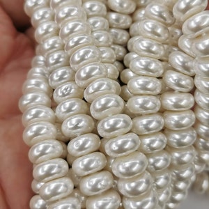 May include: A strand of white pearl beads, each bead is round and smooth with a high gloss finish. The beads are arranged in a loose coil, creating a beautiful and elegant look.
