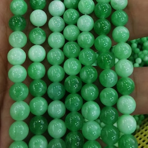 Puede incluir: Una hebra de cuentas redondas de jade verde. Las cuentas son lisas y pulidas, con una ligera variación de color de verde claro a verde oscuro.