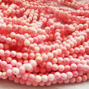 Può includere: Una collana di perle di corallo rosa. Le perle sono rotonde e lisce, e hanno un aspetto naturale e organico. Il corallo è di colore rosa chiaro, e le perle sono infilate su un filo trasparente.