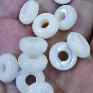 Könnte beinhalten: Eine Sammlung weißer, runder, donutförmiger Perlen mit einem Loch in der Mitte. Die Perlen sind aus einem glatten, glänzenden Material gefertigt.