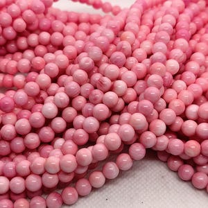 May include: Close-up of several strands of pink gemstone beads. The beads are small, round, and a soft pink colour. The strands are arranged in a loose, intertwined pattern, creating a textured and visually appealing display. Ideal for jewellery making.