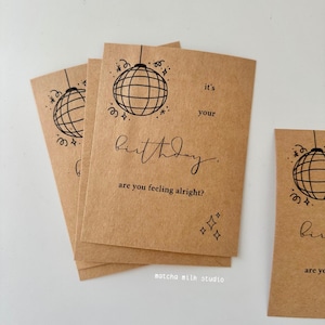 May include: Kraft paper birthday cards with a black disco ball illustration and the text "it's your birthday. are you feeling alright?" The cards also feature the text "matcha milk studio."