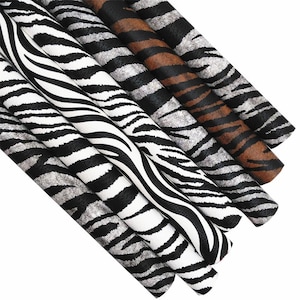 May include: A selection of rolled fabric samples featuring animal print designs. The patterns include zebra stripes in black and white, and tiger stripes in brown and black. The fabrics are arranged diagonally, displaying the range of patterns.