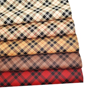 Op de afbeelding: Vijf stukken geruit stof in verschillende kleuren, waaronder beige, bruin, rood en zwart. De stof heeft een ruitpatroon.