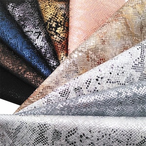 Könnte beinhalten: Eine Auswahl an Kunstlederstoffen mit Schlangenmuster. Die Stoffe sind in verschiedenen Farben erhältlich, darunter Schwarz, Blau, Silber, Gold und Rosa. Die Materialien sind gefaltet, um die verschiedenen Farben und Texturen zu zeigen.