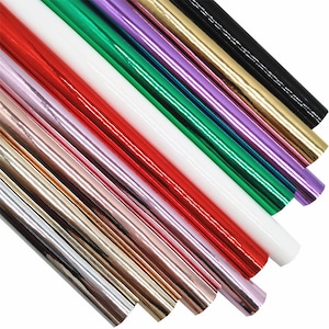 Pode incluir: Conjunto de folhas de vinil metálico em várias cores, incluindo ouro, prata, vermelho, verde, roxo e preto. As folhas estão dispostas em forma de leque, mostrando suas superfícies brilhantes e reflexivas.