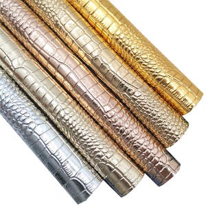 Può includere: Quattro rotoli di pelle sintetica con un motivo goffrato a coccodrilo. I rotoli sono in tonalità oro, oro rosa e argento.