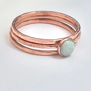 May include: A delicate copper ring with three bands and a white opal gemstone.