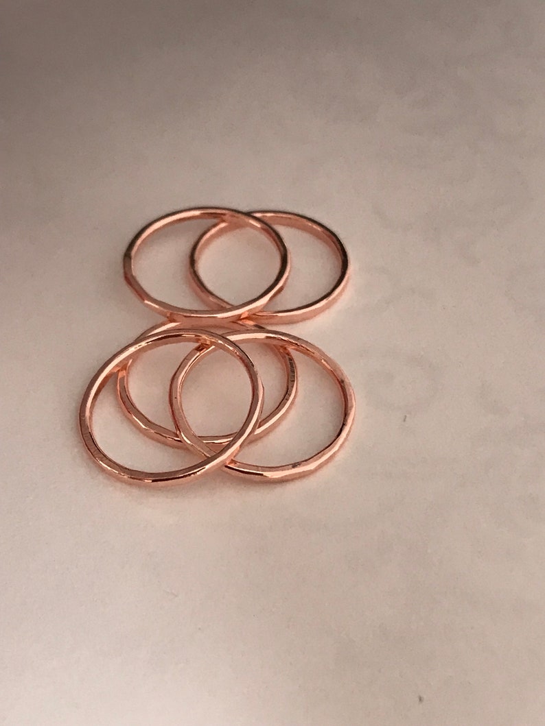 May include: Five rose gold stacking rings. The rings are simple and delicate, with a hammered texture.