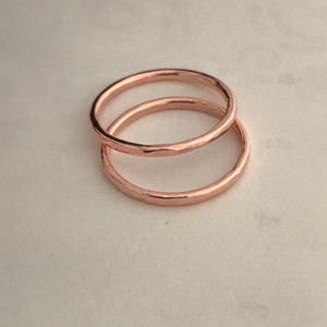 May include: Two thin rose gold rings stacked on top of each other. The rings are smooth and have a hammered texture.