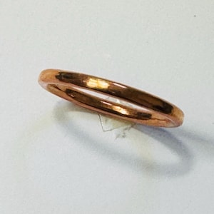May include: A copper-coloured ring with a double band design. The ring has a smooth, polished finish and reflects light, showcasing its metallic sheen. The ring is a piece of jewellery.