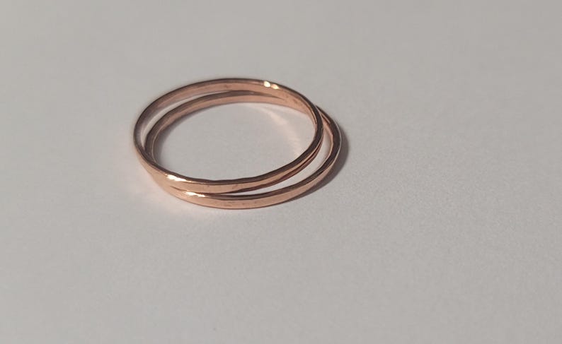 May include: Two thin, rose gold rings interlocked together. The rings are smooth and have a slightly hammered texture.