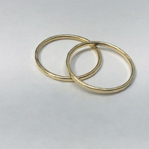 Puede incluir: Dos anillos dorados entrelazados, sobre un fondo blanco. Los anillos tienen un diseño sencillo y elegante, con una superficie ligeramente texturizada. Los anillos probablemente son de metal precioso.