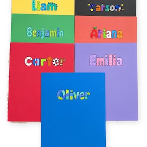May include: Seven rectangular notebooks in various solid colors including yellow, black, green, red, orange, purple, and blue. Each notebook features a personalized name printed on the front cover in colorful, patterned, and decorative lettering.
