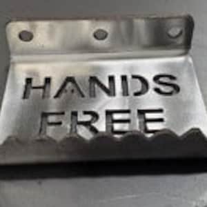 Könnte beinhalten: Ein silberner, handsfreier Türöffner aus Metall mit einer gezackten Kante und den Worten "HANDS FREE", die in die Oberfläche eingeätzt sind.