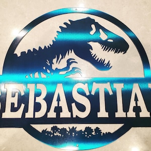 Puede incluir: Un letrero de metal azul turquesa con una silueta de dinosaurio y el nombre "EBASIA" recortado en el centro. El dinosaurio está en una pose clásica de Jurassic Park.