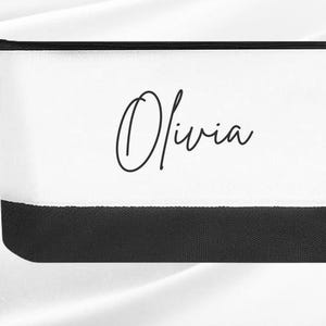 May include: White zippered pouch with a black bottom border. The pouch has the name "Olivia" written in black cursive on the front.