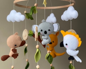 May include: A wooden baby mobile with felt animal toys, including a koala, a platypus, a kangaroo, and a cockatoo. The mobile also features clouds and green leaves.