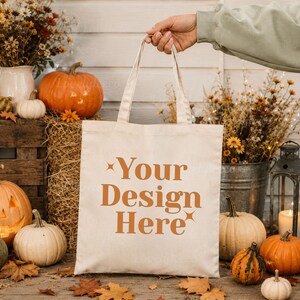 May include: A cream-colored canvas tote bag with two handles, featuring the text "Your Design Here" printed in a bold, burnt orange serif font, accented by small four-pointed star symbols on the top left and bottom right of the text.