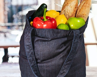 May include: A dark blue denim tote bag filled with groceries, including lemons, limes, green apples, a red bell pepper, cucumbers, and baguettes. The bag has a red label with the text "KHAN KUB"