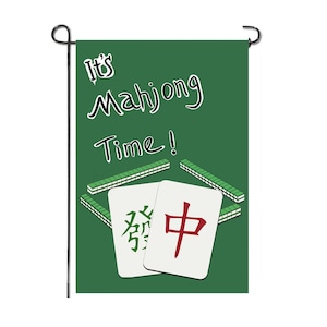 May include: A green garden flag with the text "It's Mahjong Time!" in white script. The flag features illustrations of Mahjong tiles and stacks on a green background. The flag is attached to a black metal pole.