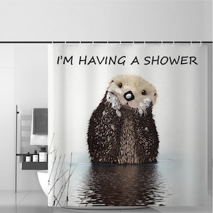 Könnte beinhalten: Duschvorhang mit einem Cartoon-Otter im Wasser, mit dem Text "I'M HAVING A SHOWER". Der Otter hat braunes Fell und ist mit Blasen bedeckt. Das Wasser hat eine reflektierende Oberfläche.
