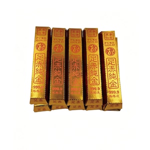 Pode incluir: Várias barras douradas com embalagem vermelha e dourada empilhadas. A embalagem apresenta caracteres chineses e as palavras "PURE GOLD" e "999.9". As barras são provavelmente uma forma de investimento ou um item decorativo.
