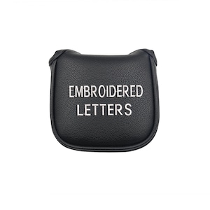 Puede incluir: Funda negra para la cabeza del palo de golf con las palabras "EMBROIDERED LETTERS" bordadas en blanco. La funda tiene una forma redondeada y está hecha de un material texturizado.