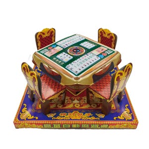 Può includere: Un set in miniatura composto da un tavolo da mahjong quadrato e quattro sedie abbinate, caratterizzato da tonalità oro e rosso. La superficie del tavolo mostra tessere del mahjong stampate e caratteri cinesi. La base presenta motivi dorati.