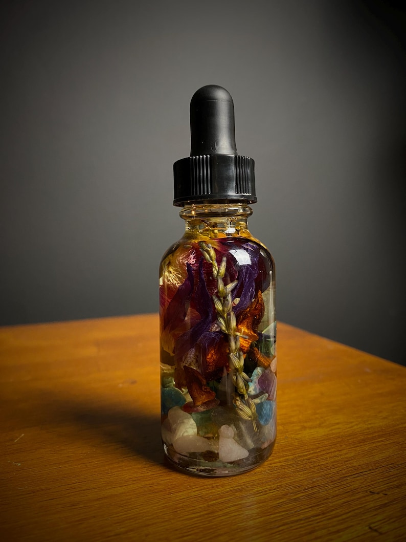 May include: A clear glass bottle with a black dropper top filled with a golden liquid and colorful dried flowers and crystals.