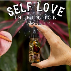 May include: A clear glass bottle filled with oil and botanicals, held in a hand. The bottle has a black dropper and is labeled "SELF LOVE INTENTION OIL". A pink flower and green foliage are in the background.