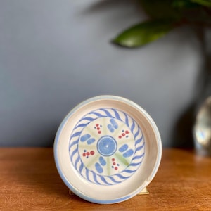 May include: A white ceramic bowl with a blue and green swirl design and red accents. The bowl is circular and has a slightly raised rim.