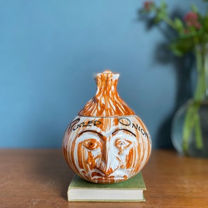 May include: A white ceramic onion-shaped jar with a brown glaze and the words "Dried Onion" written on it. The jar has a face with painted eyes, nose, and mouth.