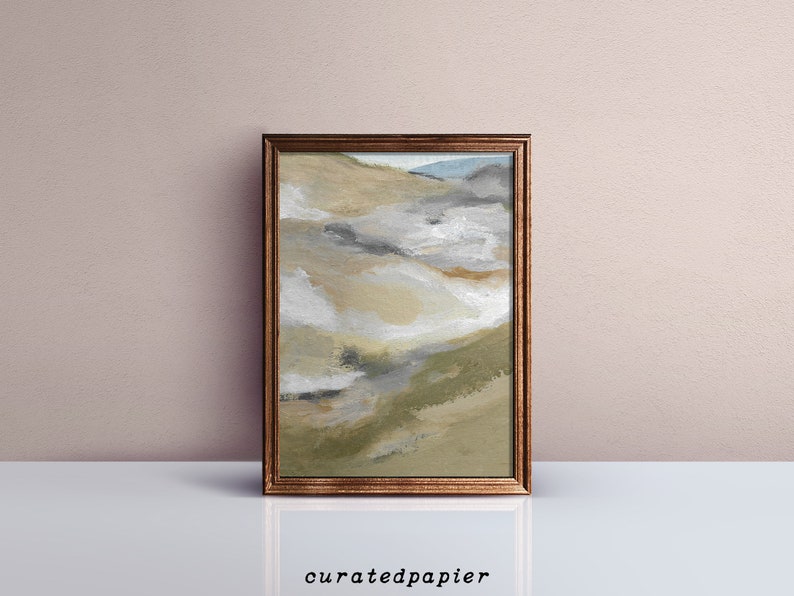 May include: Abstract landscape painting in a brown wooden frame. The artwork features a blend of beige, gray, and green hues, evoking a sense of nature. The bottom of the frame rests on a white surface, with the text "curatedpapier" at the bottom.