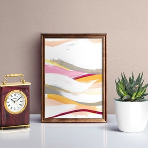 May include: A framed abstract painting with a white background and colorful brushstrokes in shades of pink, yellow, orange, and gray. The frame is a dark brown wood.