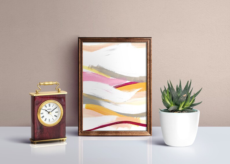 May include: A framed abstract painting with a white background and colorful brushstrokes in shades of pink, yellow, orange, and gray. The frame is a dark brown wood.