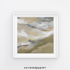 May include: Abstract art print in a white frame. The artwork features a landscape-inspired design with beige, white, gray, and olive green brushstrokes. The text "curatedpapier" is printed in black at the bottom of the frame.