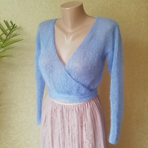 Può includere: Un cardigan blu chiaro a maniche lunghe e aperto sul davanti, con uno stile avvolgente. Il cardigan è realizzato in un tessuto a maglia morbido e delicato.