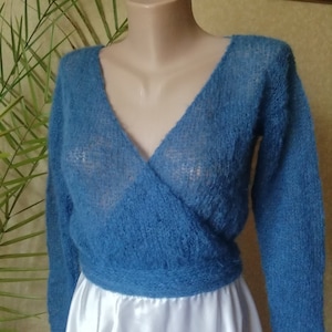 Pu&ograve; includere: Un maglione a portafoglio blu a maniche lunghe con un profondo scollo a V e una consistenza lavorata a maglia soffice e semi-trasparente. Il capo &egrave; aderente in vita con una fascia larga ed &egrave; esposto su un manichino, mostrando la trama aperta.