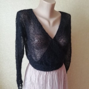Pu&ograve; includere: Un maglione a portafoglio nero a maniche lunghe caratterizzato da una trama a maglia aperta e trasparente con un profondo scollo a V. Il capo &egrave; corto in vita ed &egrave; esposto su un manichino, abbinato a una gonna plissettata rosa chiaro.